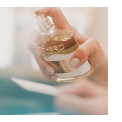 Hand holding a Creed Aventus Cologne perfume bottle with text reading CREED and AVENTUS COLOGNE.