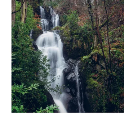 A tall waterfall cascades down rocky tiers surrounded by trees and moss in a forest.