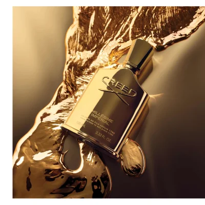 A golden Creed perfume bottle lies on a surface with molten gold, showing the text CREED MILLÉSIME IMPÉRIAL DE PERE EN FILS DEPUIS 1760 FROM FATHER TO SON SINCE 1760 100 ML 3.33 FL. OZ.