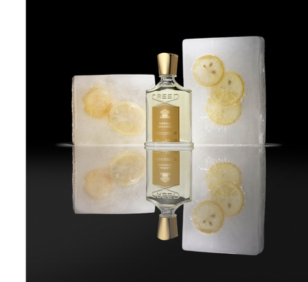 A Creed Neroli Sauvage perfume bottle is positioned between two ice blocks containing frozen lemon slices, reflected on a dark surface, with the text CREED NÉROLI SAUVAGE PÈRE EN FILS DEPUIS 1760 FROM FATHER TO SON SINCE 1760 100ML 3.33 FL.OZ visible on the bottle.