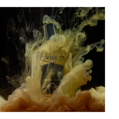 A Creed Royal Oud perfume bottle is surrounded by swirling yellow and brown liquid against a black background, with text on the bottle reading CREED ROYAL OUD DE PERE EN FILS DEPUIS FROM FATHER TO SON SINCE 100ML 3.3 FL.OZ.