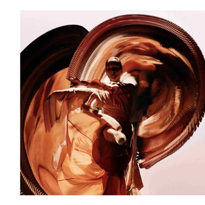 A person wearing an intricate orange pleated costume with large fan-like structures around their body