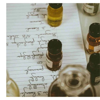 Small glass bottles containing liquids sit on a sheet of paper with handwritten notes including 3 Resorcin Citronellol Linalool Paracresol CD Phenylactique muguet Eucalyptus Phénylacétique 5 Bergamot 3 Ris Italia S/B Jakon th benzyle 24 NCE.
