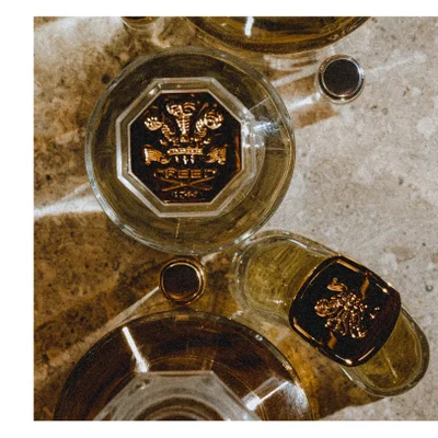 Overhead view of several perfume bottles, with one prominent round bottle label featuring a gold crest and the text CREED 1760.