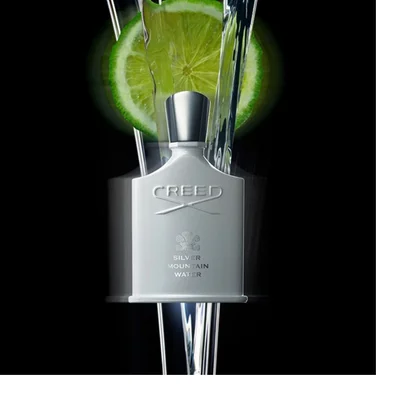 A collection of Creed Silver Mountain Water products, featuring a white bar soap embossed with CREED 1760, two light-colored pump bottles with gold caps labeled CREED 1760 SILVER MOUNTAIN WATER BAIN & BODY WASH and CREED 1760 SILVER MOUNTAIN WATER HAND & BODY LOTION respectively, and a white perfume bottle with a silver cap displaying CREED SILVER MOUNTAIN WATER, all presented on a black reflective surface with shimmering gold liquid.